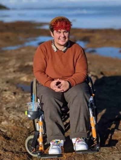 A photo of Mac, a young wheelchair user, sitting in his wheelchair by the ocean.