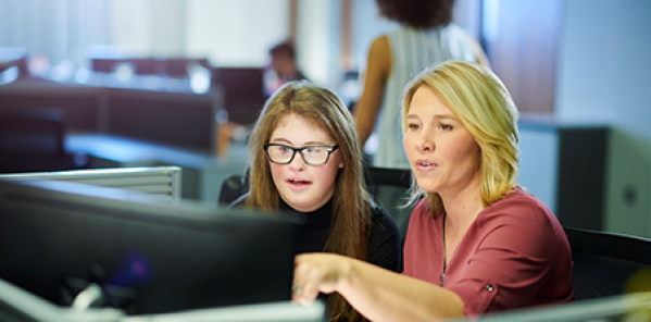 Two people looking at a computer. Blonde woman, brunette girl with glasses