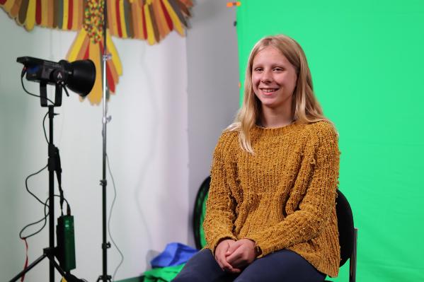 River, a blonde teenager, smiling while sitting in front of a green screen