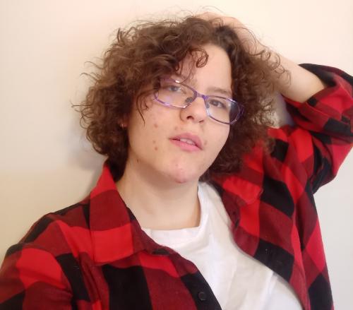 White teen wearing glasses & flannel shirt, short brown hair, right arm on head 