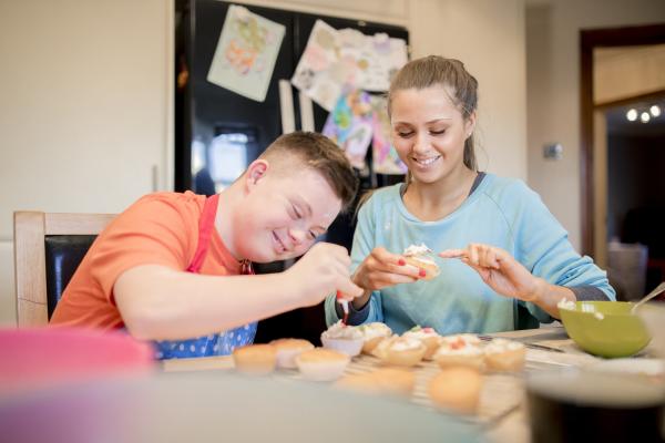 Boy with Down syndrome making cupcakes with a smiling woman 
