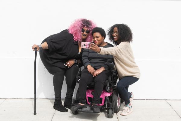 Three people taking a selfie. Middle person using wheelchair, left using a cane