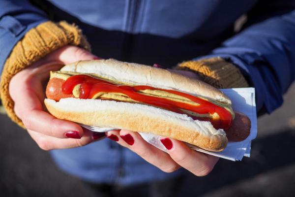 Hands holding a sausage with sauce and mustard