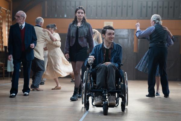 two people walking through a hall, boy in wheelchair, girl behind 