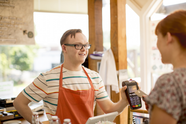 A young person with Down syndrome working at a cafe holds out an eftpos machine