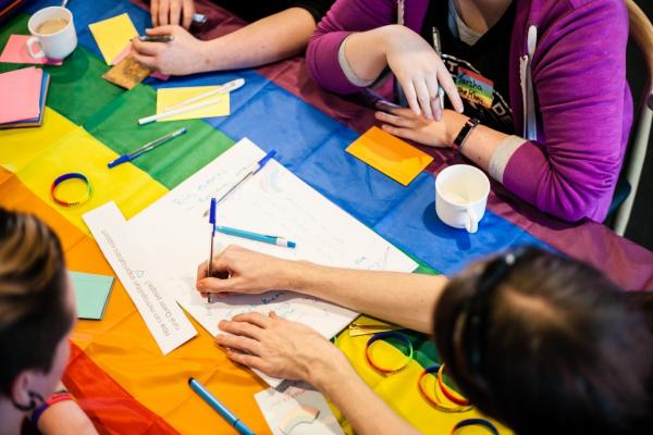 image of young people sitting around rainbow table with pens and paper.