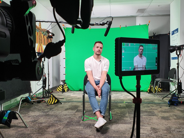 Nathan, a young person who is Deaf, sitting near a camera and green screen.