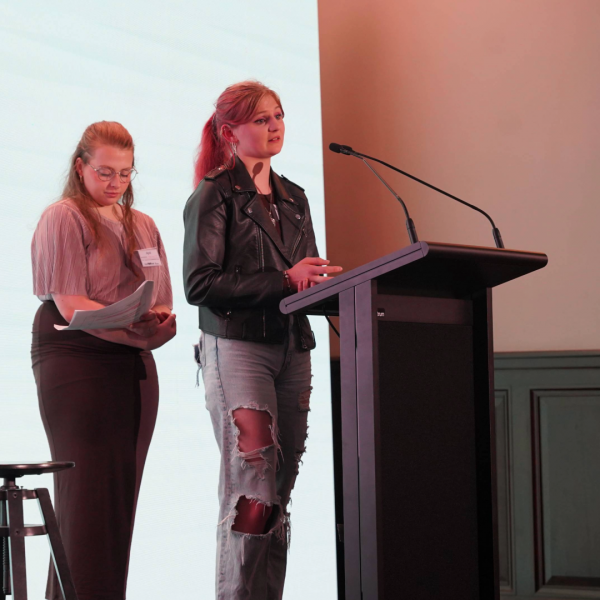 Two young people on stage, behind a podium, giving a speech at a conference.