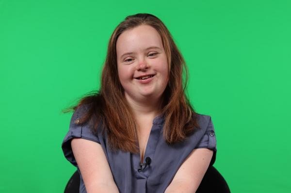 Ashleigh, a young person with Down syndrome, smiling in front of a green screen